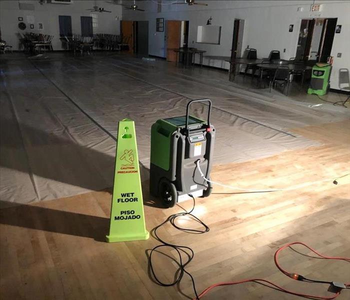 Plastic laid down on damaged area with a dehumidifier running and a "Caution, Wet Floor" sign beside it.