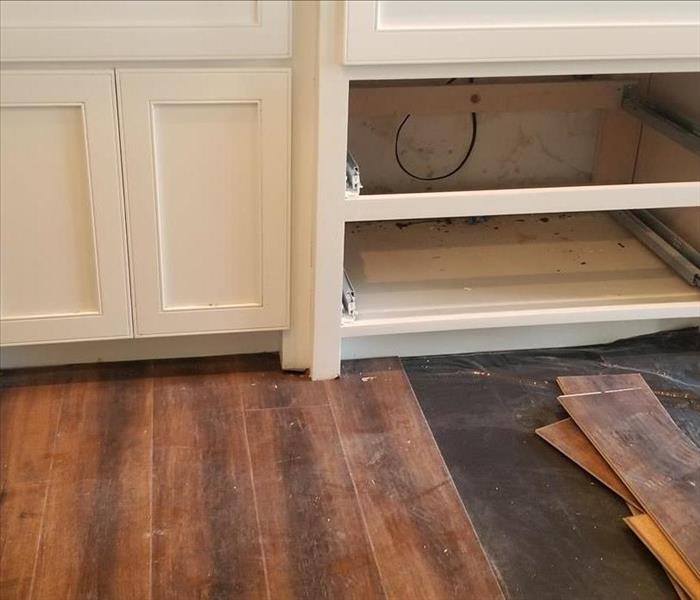 Partially removed flooring by kitchen cabinets.